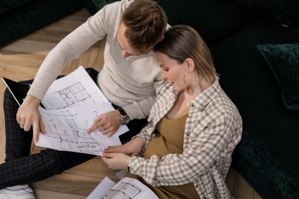 Couple sitting together on the floor, discussing house plans and reviewing architectural drawings.