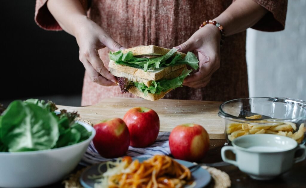 Person holding sandwiches with lettuce over a table with apples, salad, and fries.
