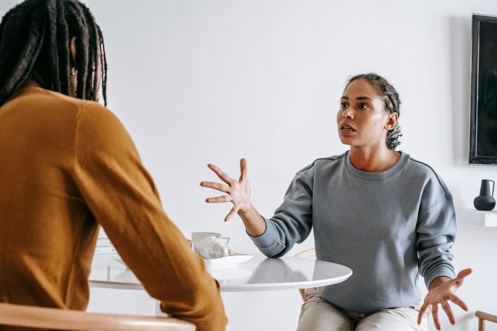 Woman gesturing with both hands while speaking to another person across a small round table.