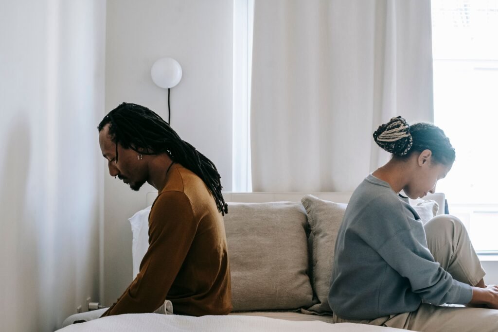 Two adults sit back to back on a sofa, each looking down.