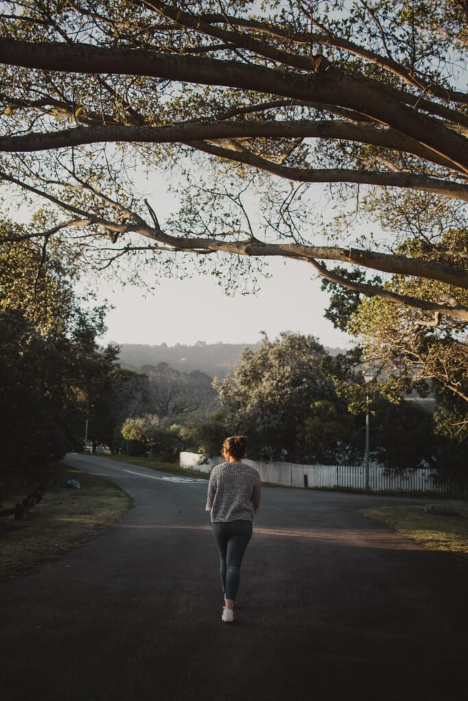 A woman walks alone along a quiet residential road beneath overhanging tree branches.