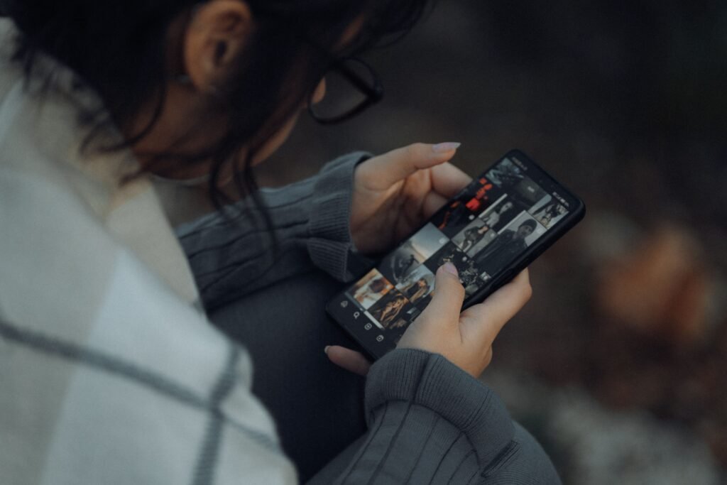 Woman wearing glasses browsing a grid of photos on her smartphone.