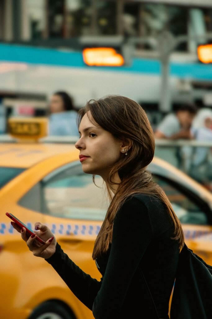 Woman holding a phone on a city street beside a yellow taxi