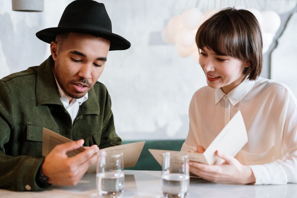 Man and woman sitting across from each other at a café table, smiling while reading menus together.