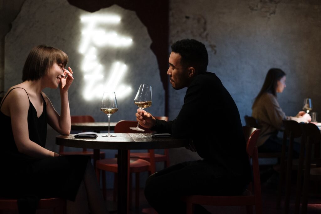 Woman smiling across a restaurant table at a man holding a wine glass.