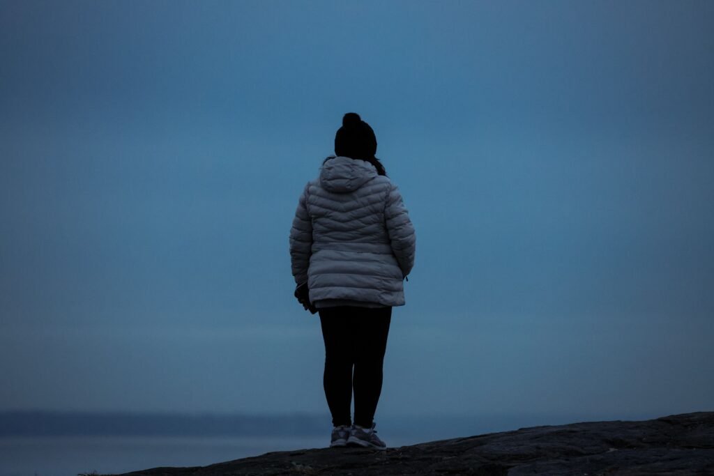 A person in a light jacket stands on rocky ground beneath a blue-gray sky.