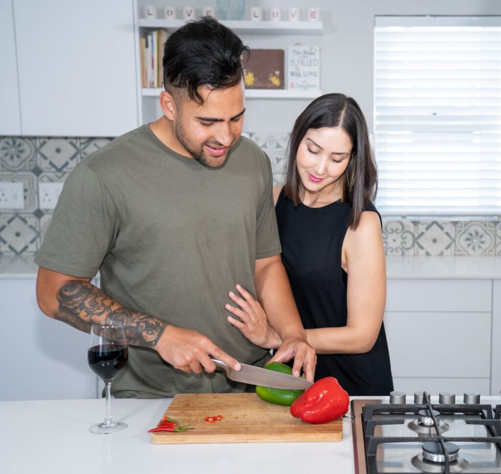 A man slices a green pepper while a woman stands beside him at a kitchen counter.