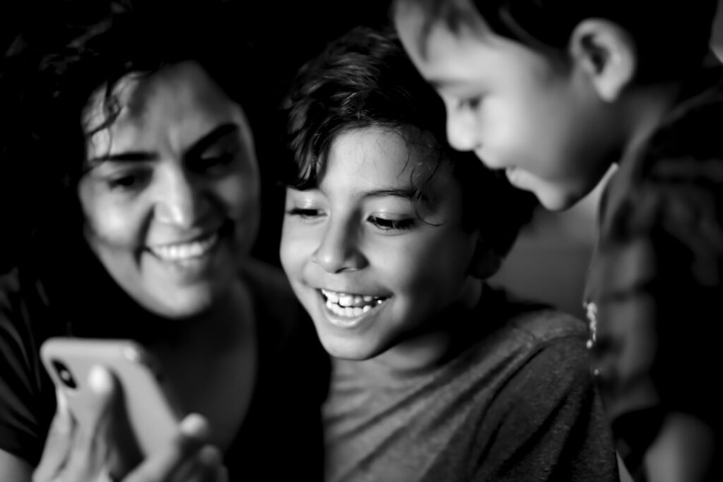 Mother smiling with her two children as they look at a smartphone together, sharing a happy family moment.