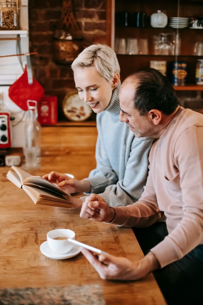 Two people looking at an open book together at a kitchen table
