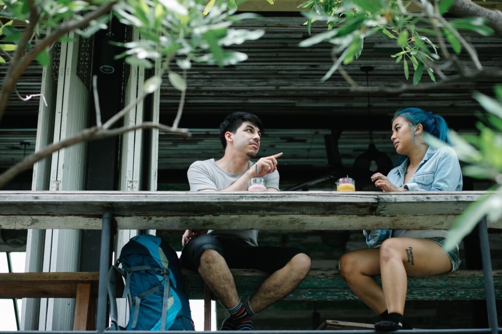 A man gestures while speaking to a woman across an outdoor table.