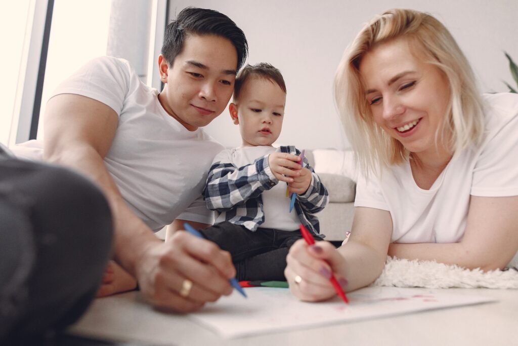Man and woman drawing with colored pencils beside a toddler holding pencils.