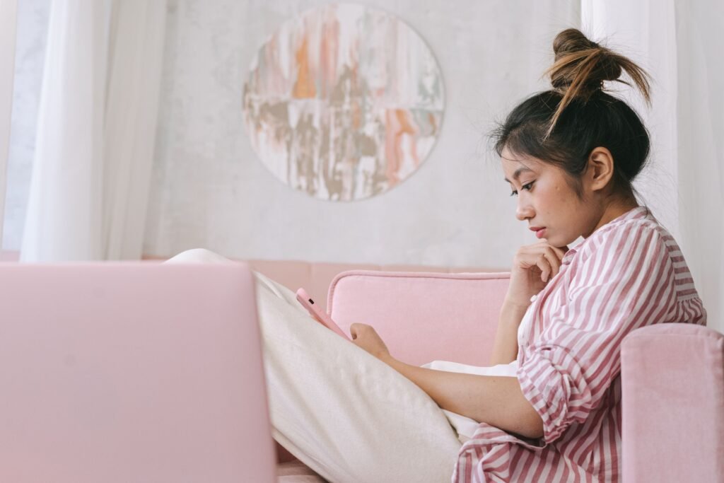 Thoughtful woman sitting alone on a pink sofa, looking down at her phone.