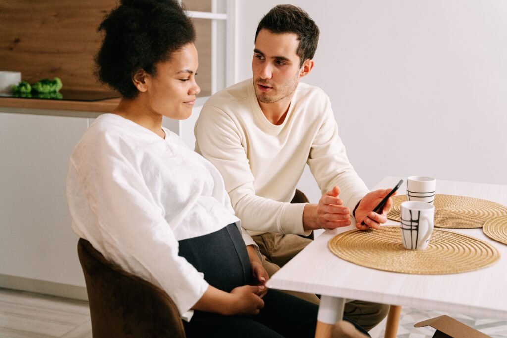 A man holding a smartphone talks with a woman at a kitchen table.