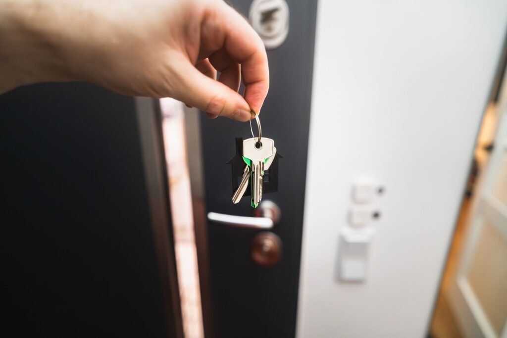 Close-up of a hand holding house keys with a house-shaped keychain in front of an open door.