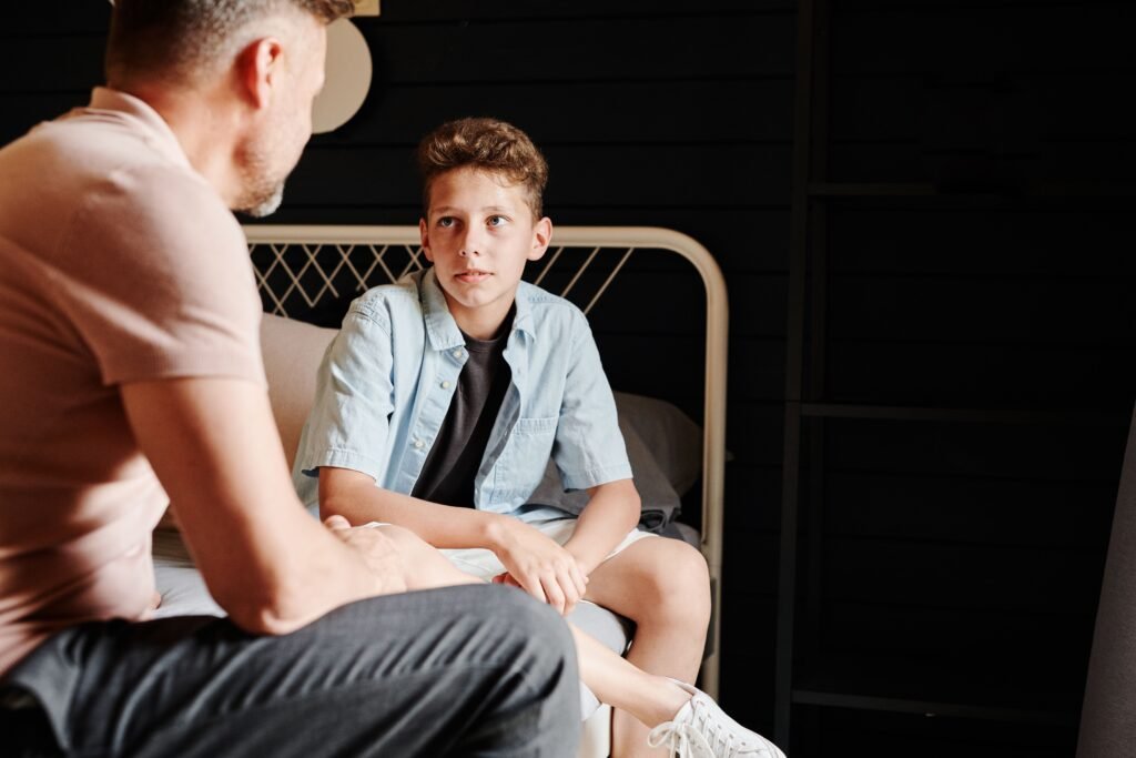 Boy seated on a bed, looking up at a man sitting beside him.