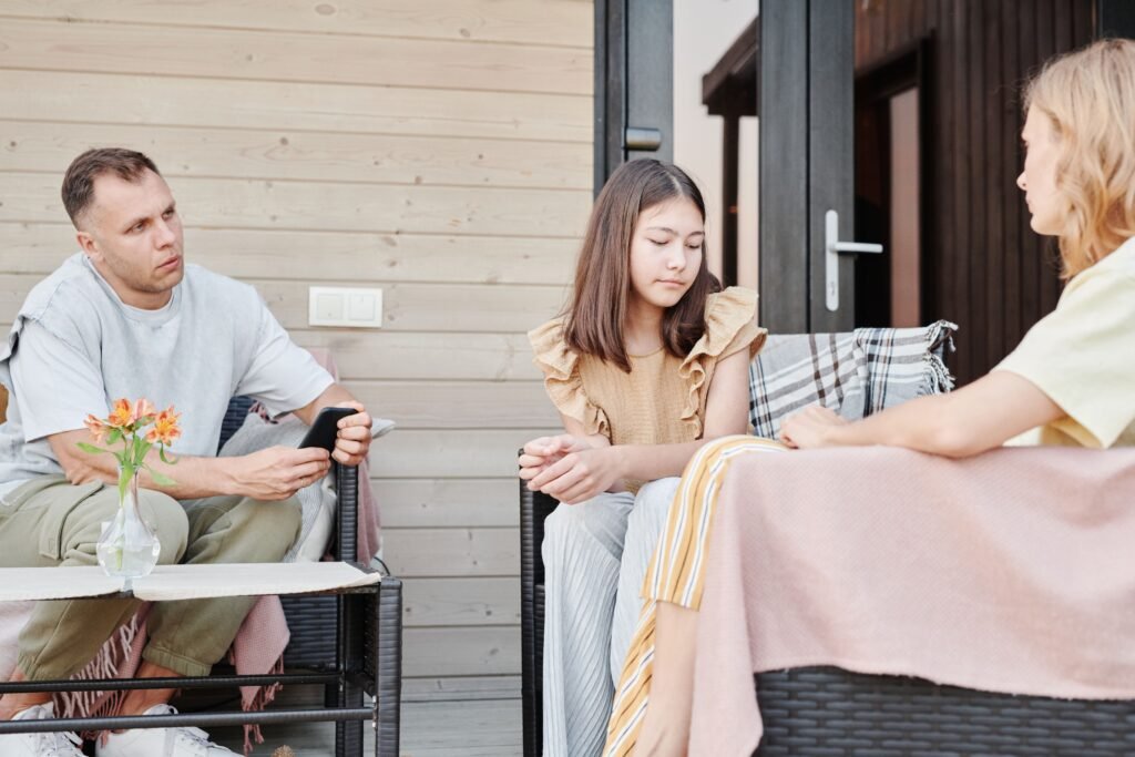 Man and woman seated with a girl between them during a conversation outdoors.