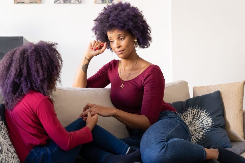 Mother sitting on a sofa and holding her daughter's hands while listening attentively during a heartfelt conversation at home.