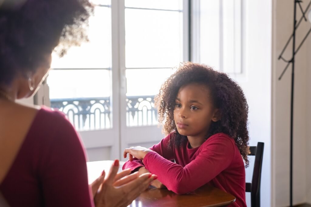 Girl sitting at a table, listening to a woman who gestures while talking.