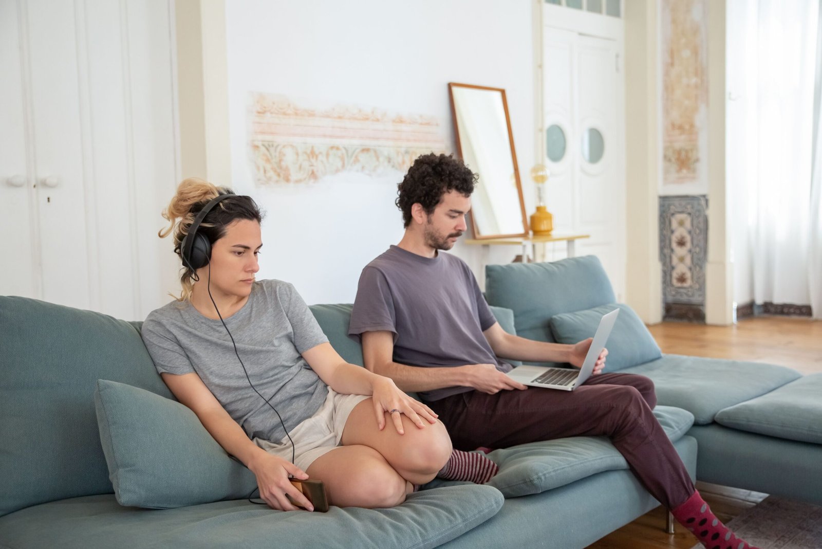 Two people sit apart on the same sofa in a bright living room.