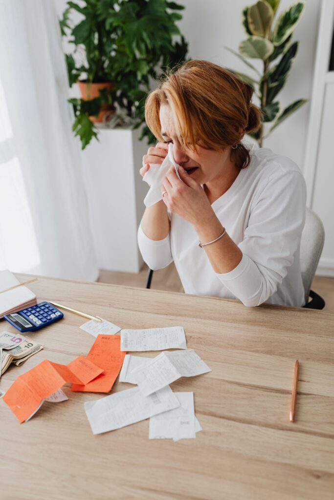 Woman sitting with her hands near her face at a table covered with receipts and a calculator