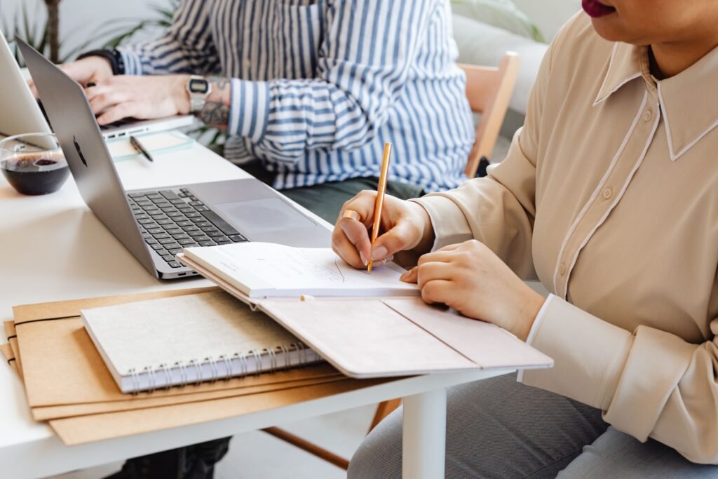 Person writing in a notebook beside a laptop