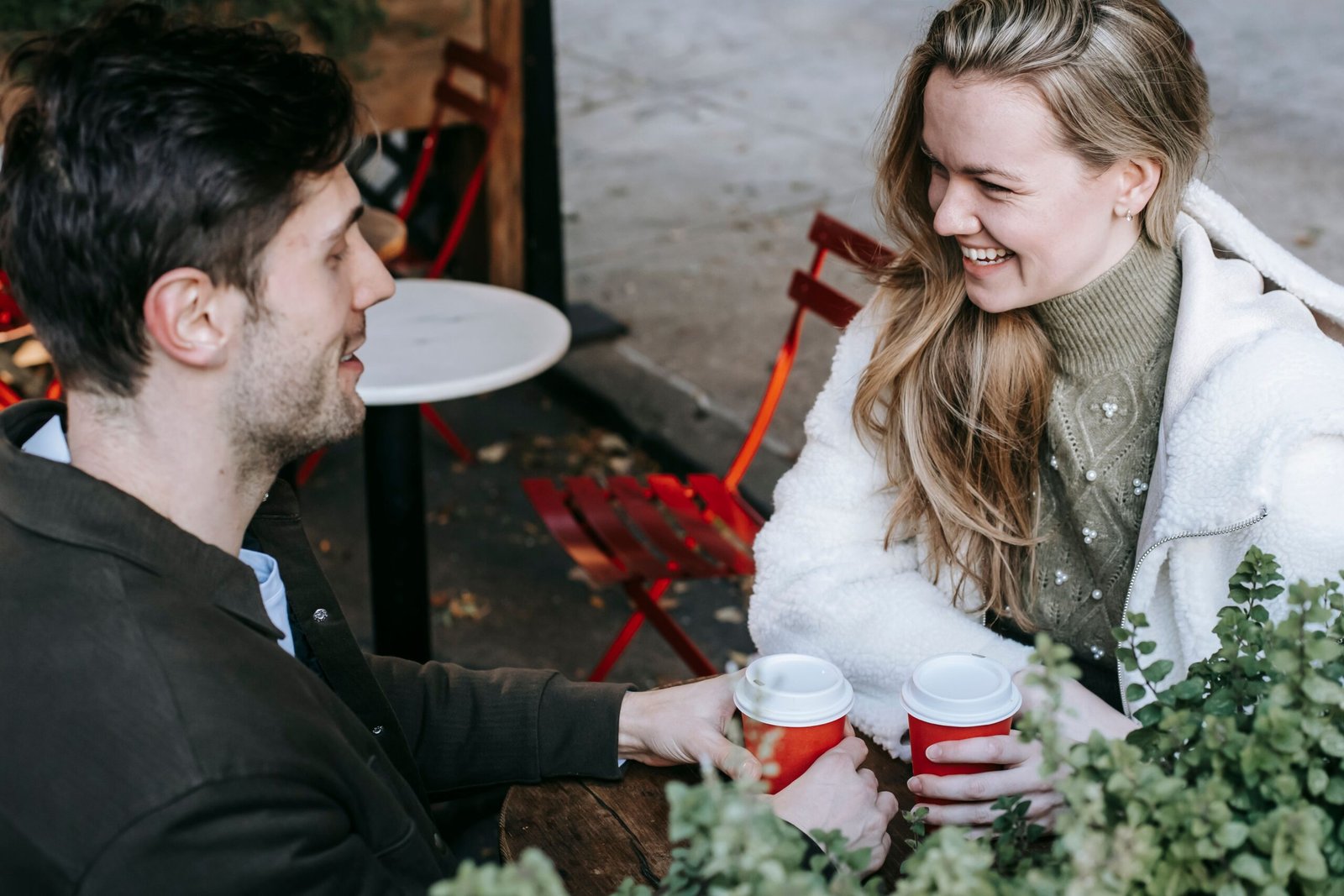 Two people smile while talking over coffee outdoors.