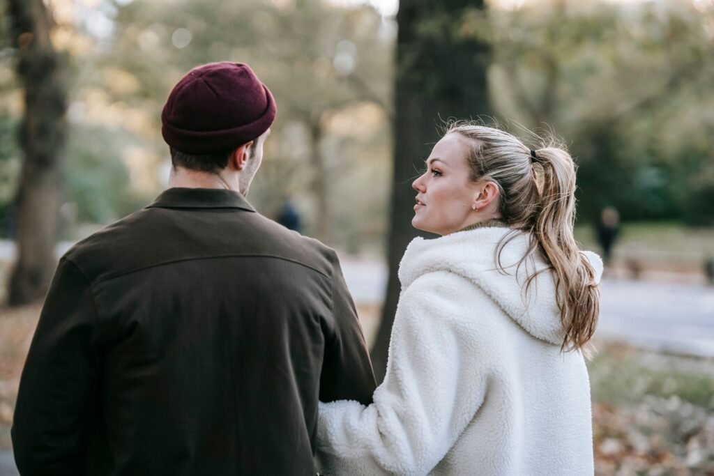 Couple walking together through a park, with the woman holding the man's arm while talking to him.