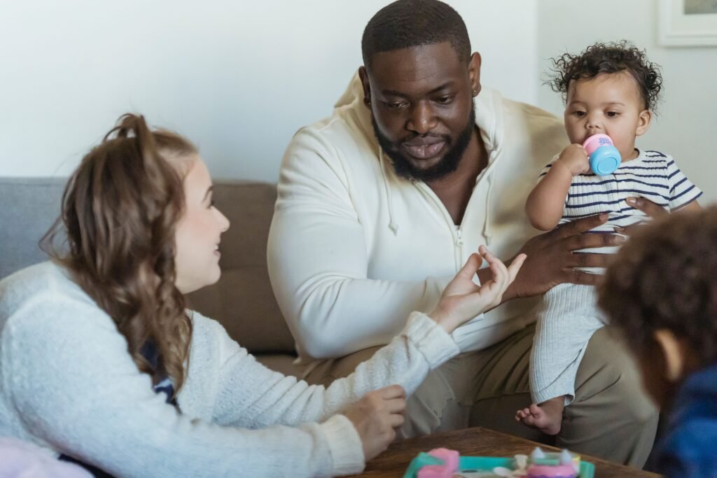 Man holding a toddler while two children gather around him at home.