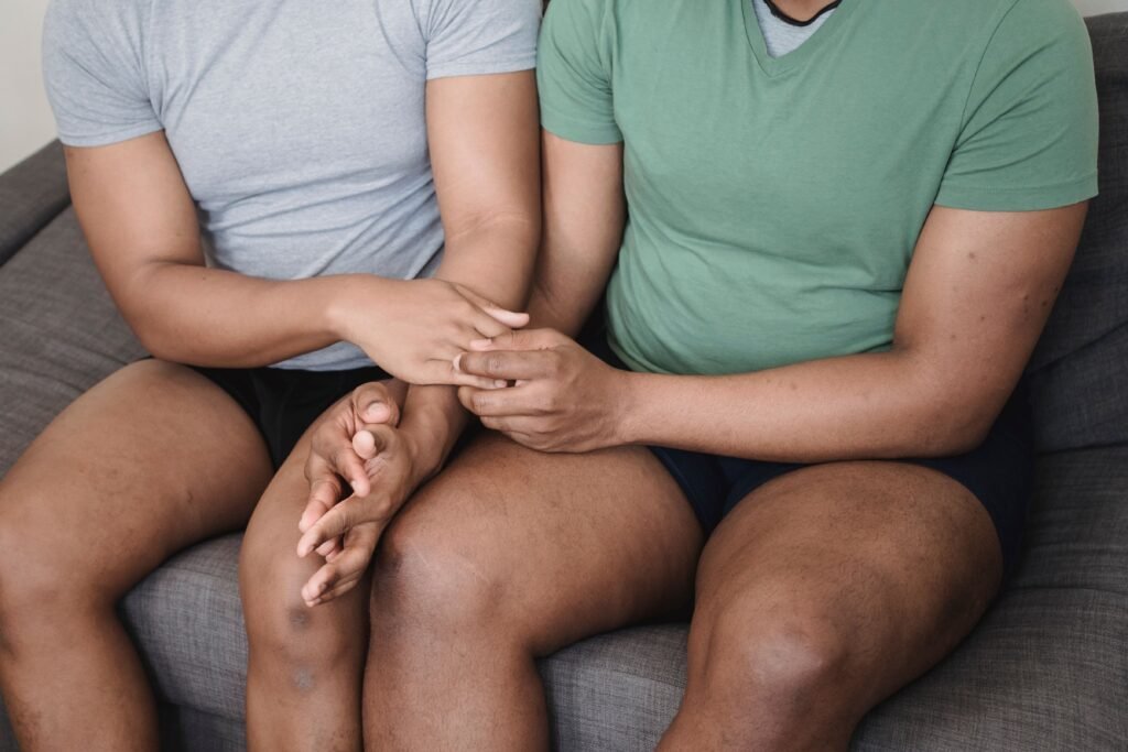 Close-up of two people sitting side by side on a sofa, gently holding hands in a comforting and supportive gesture.