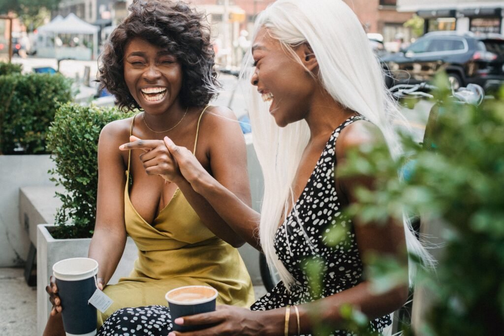 Two women laughing together outdoors while holding takeaway drink cups.