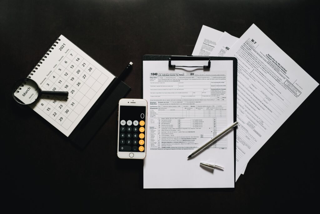 A calendar, phone calculator, pen, and tax forms arranged on a dark desk.