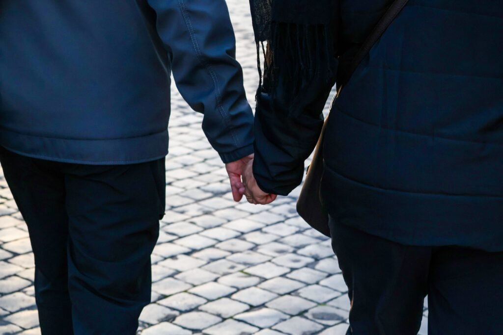 Close-up of two people holding hands outdoors on a cobblestone path.