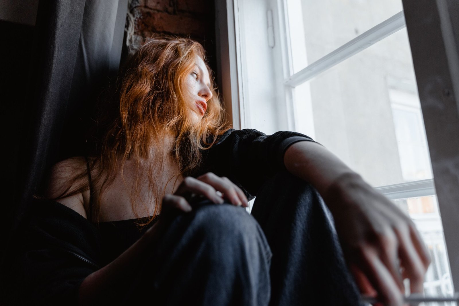 A woman sits by a window looking outside.