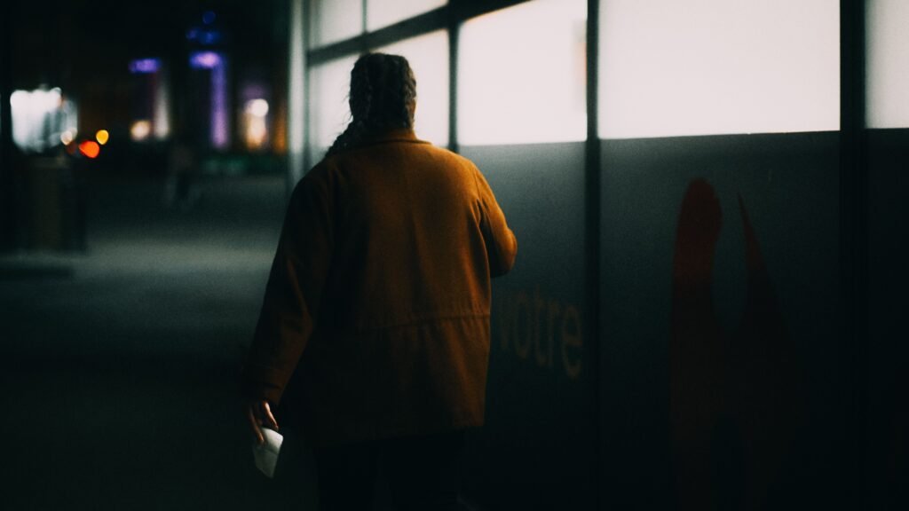 Woman in a brown jacket walking along a dimly lit street at night