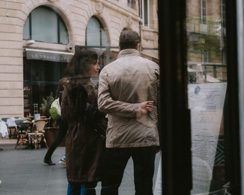 A woman and a man look at a menu outside a café on a city street.