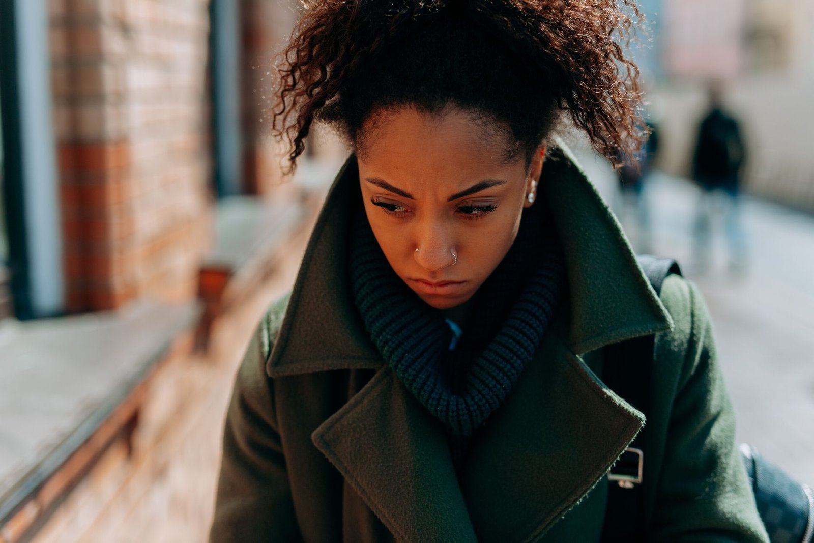 A woman in a green coat looks down while walking outside.