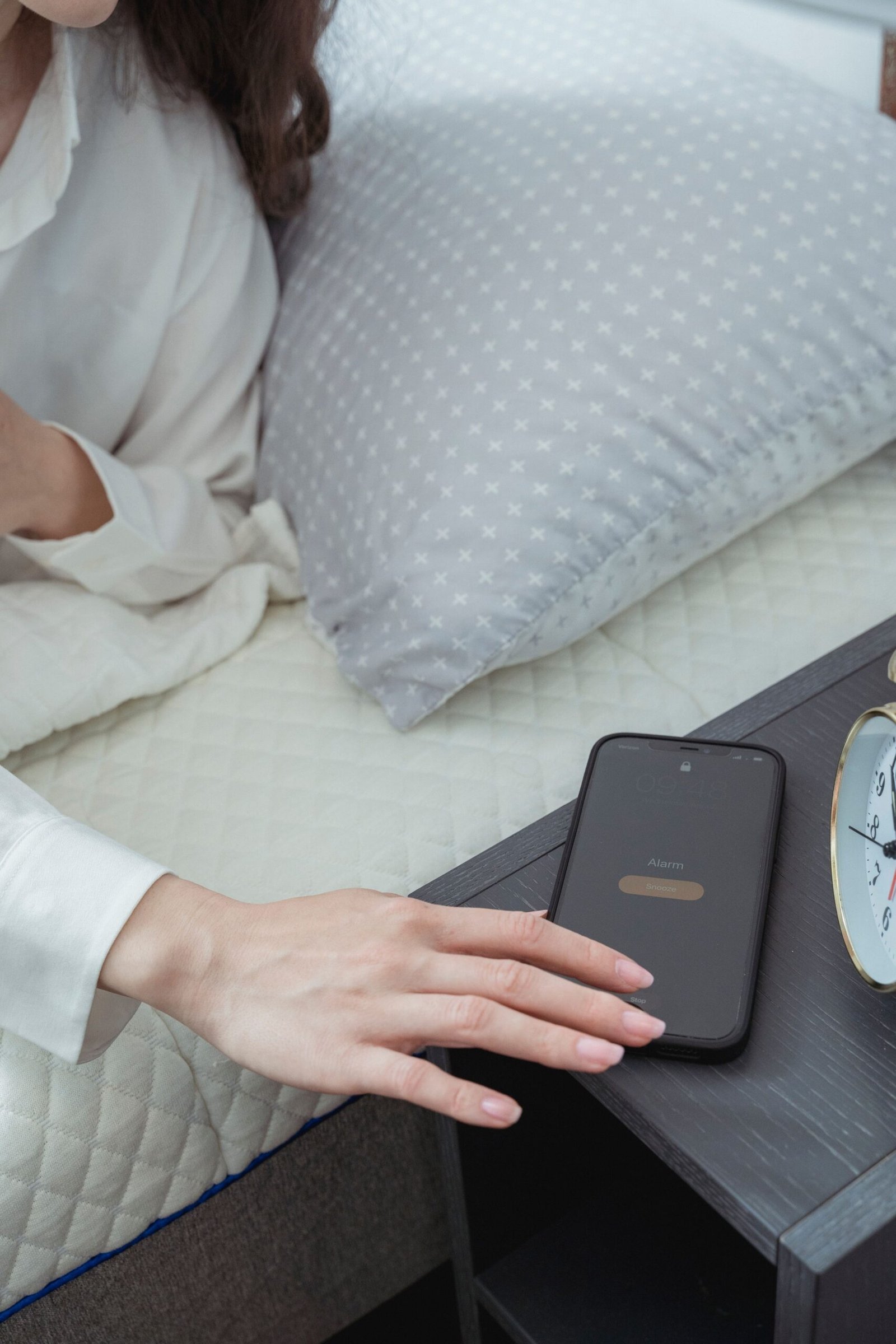 A hand reaches toward a phone resting beside a bed.