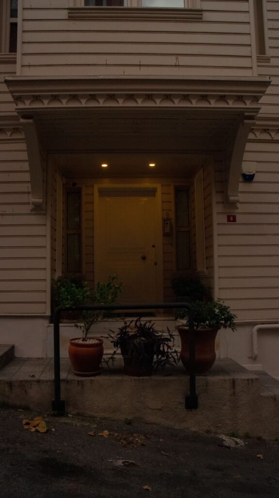 Closed building entrance at dusk with overhead lights and potted plants.
