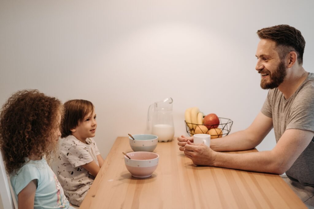 Man smiling and talking with two children at a dining table.