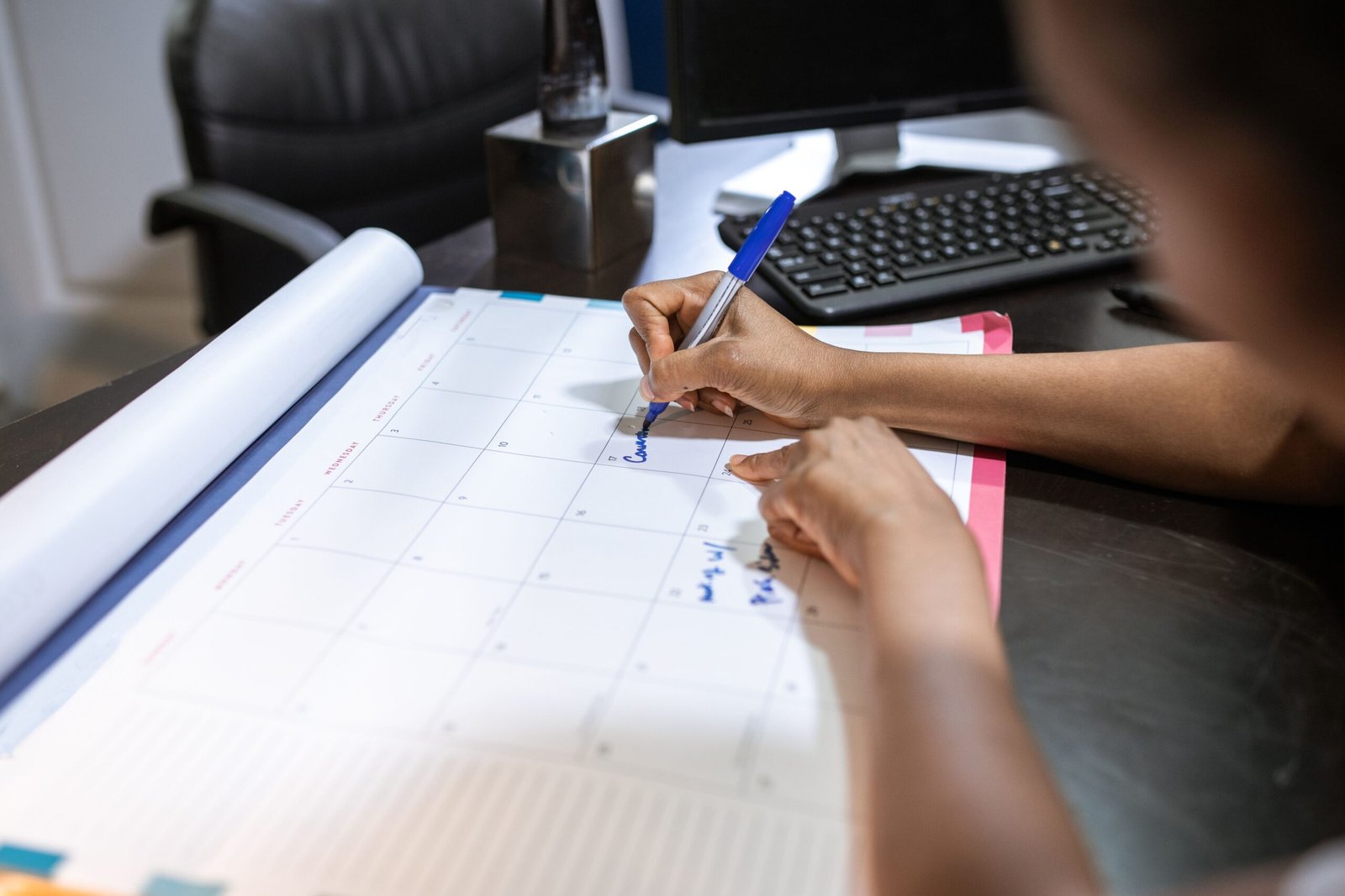 Hands write on a paper calendar at a desk.