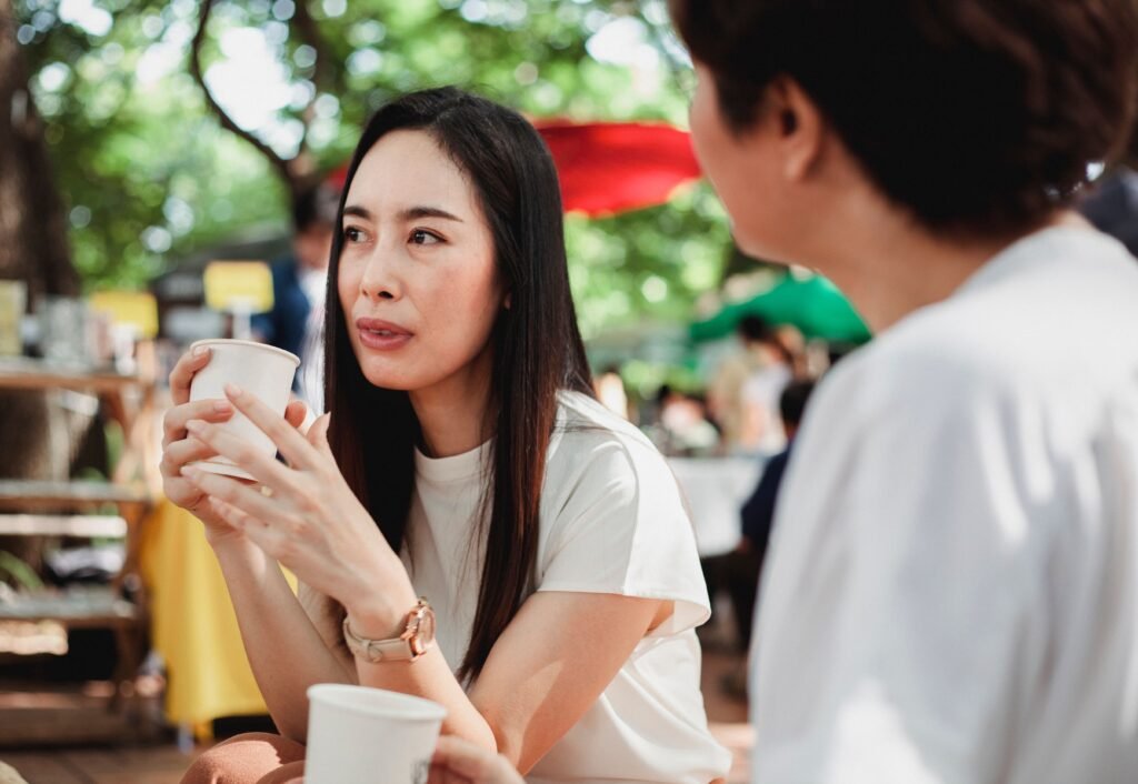 A woman holding a cup talks with another person at an outdoor café.