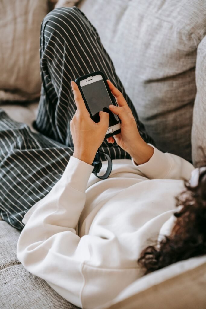 Person reclining on a grey sofa while holding a smartphone with both hands.