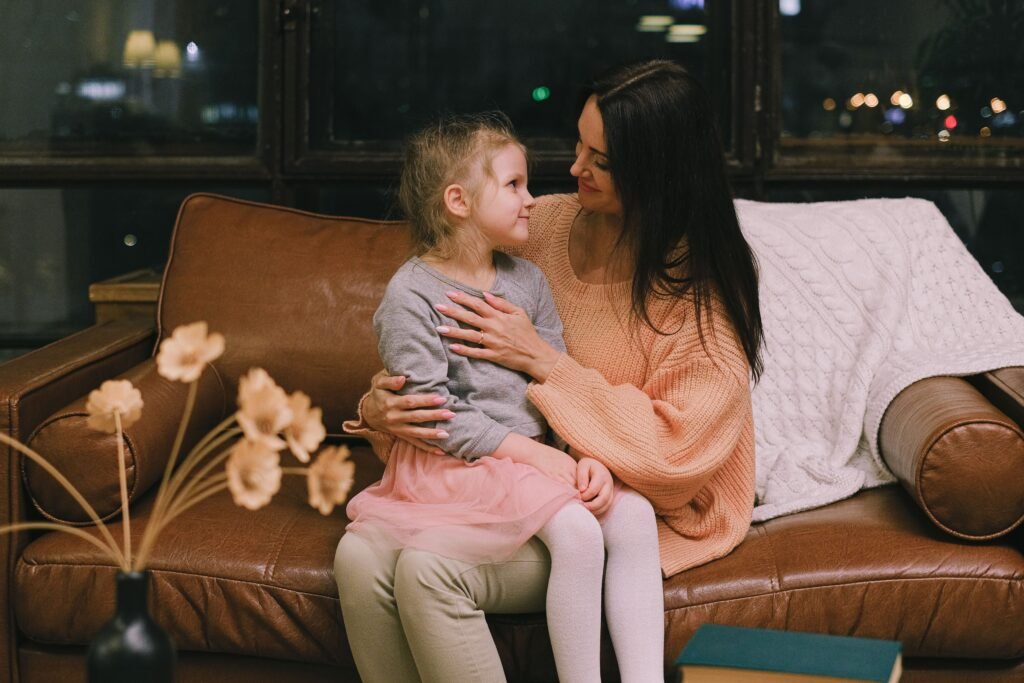 Woman holds a young girl close as they look at each other on a sofa at night.