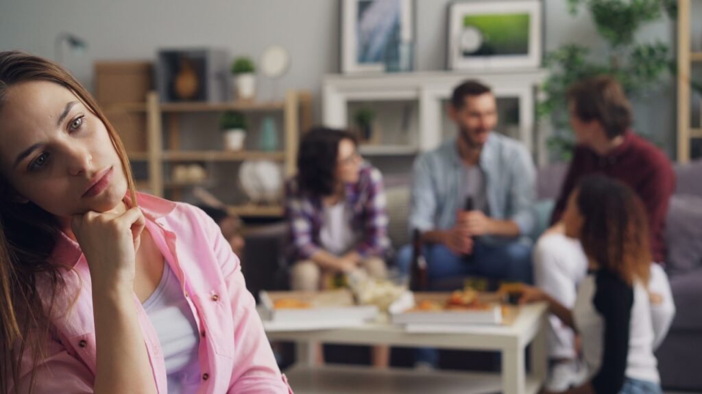 Woman sitting apart while a group talks in the background