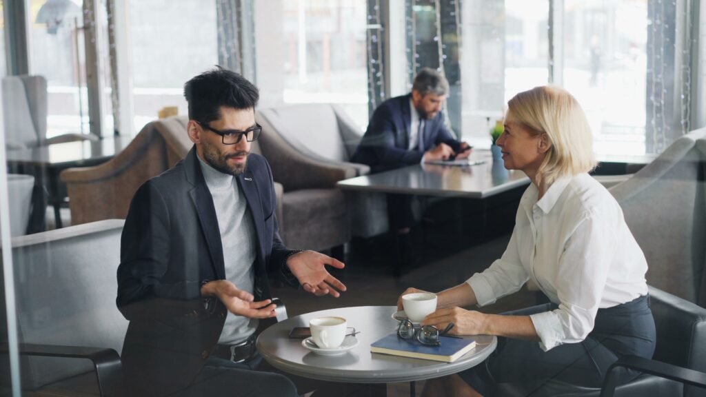 A man gestures while speaking with a woman across a café table.
