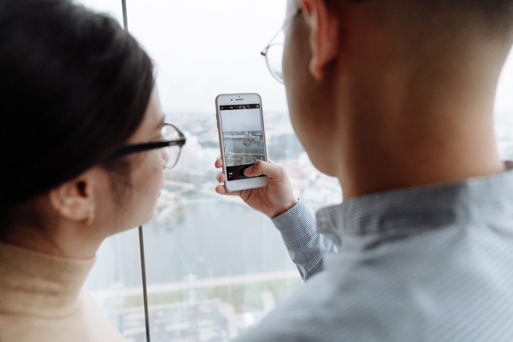 Man photographing a city view through a window with his smartphone while a woman watches beside him.