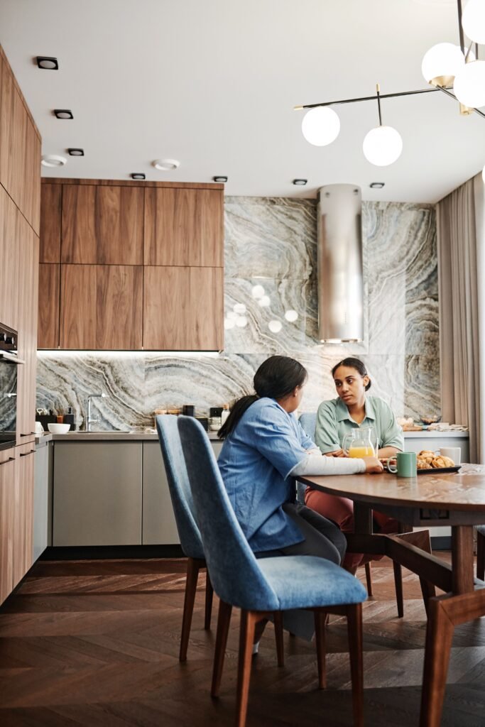 Two people talking across a dining table in a kitchen