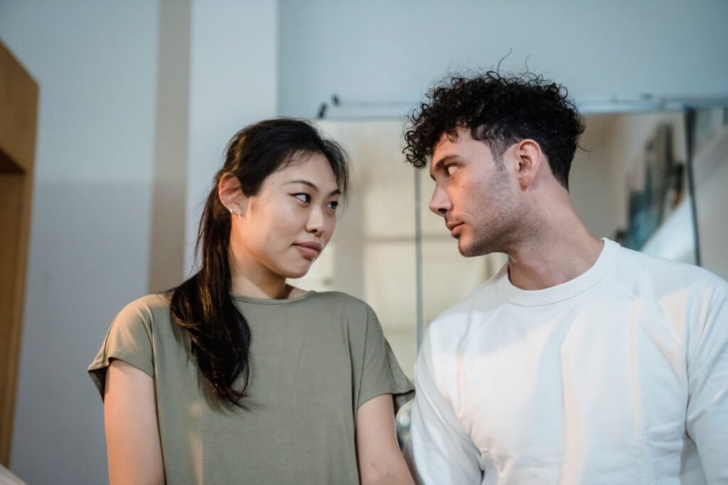 A woman and man look at each other while standing together indoors.