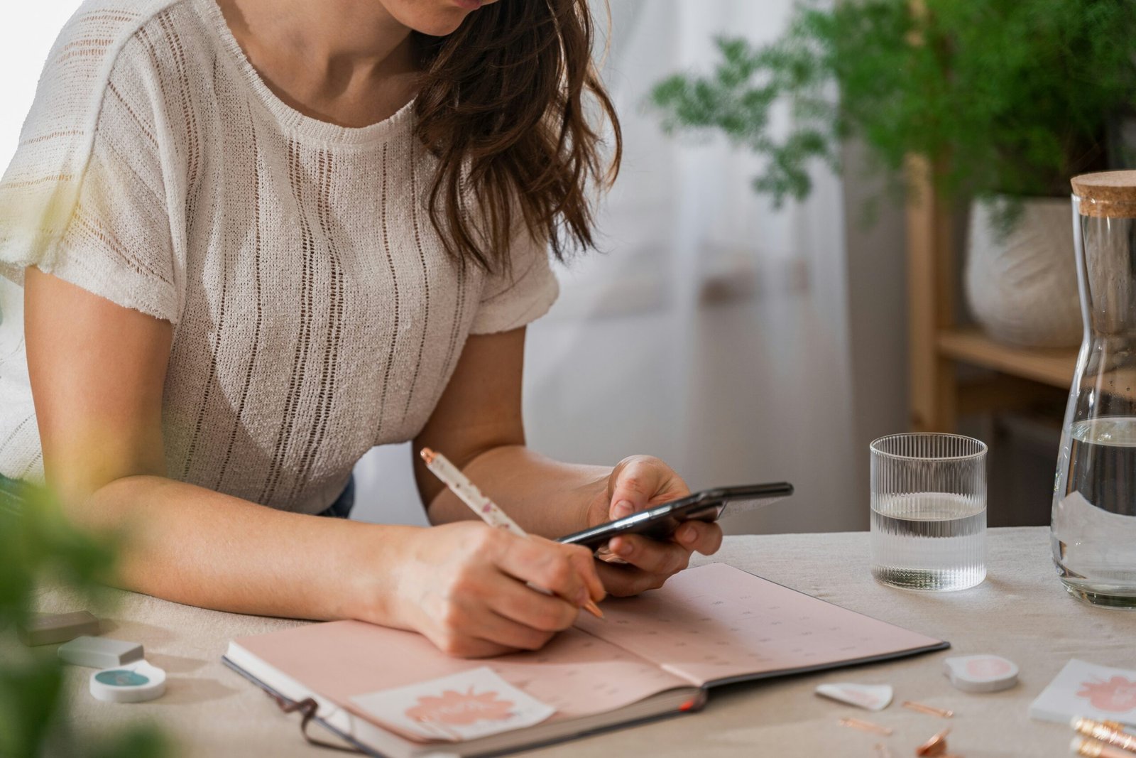 A woman holds a phone beside an open notebook on a table.