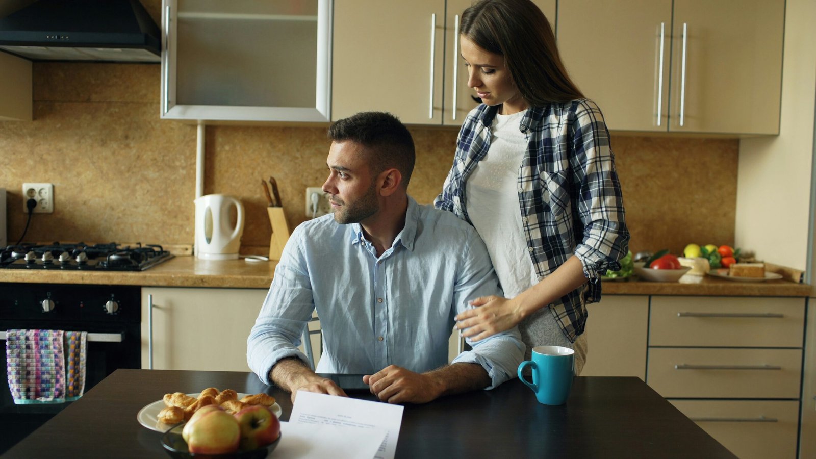 A couple stands together in a kitchen while looking in different directions.